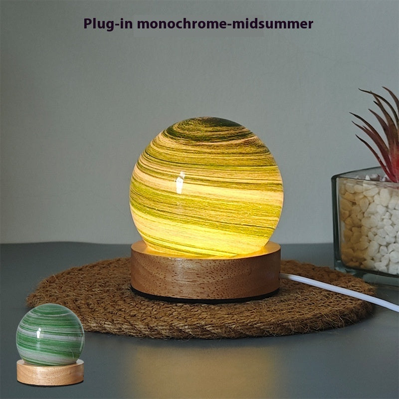 Planet night light in Midsummer, a marbled glass globe lit warm on a wooden base