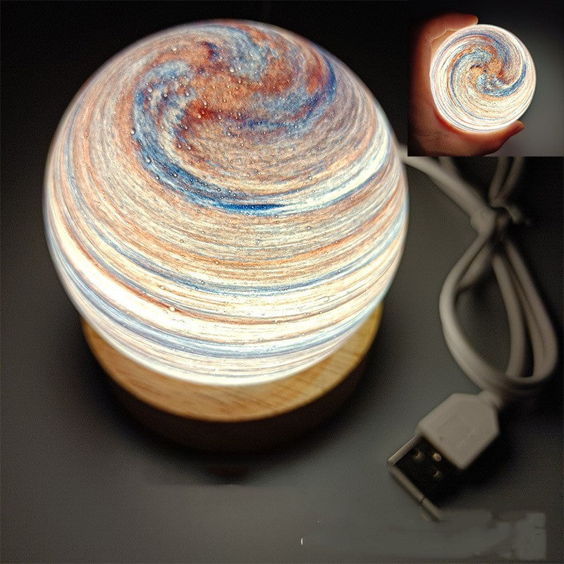 Planet night light in Sunset Glow, a marbled glass globe lit warm on a wooden base