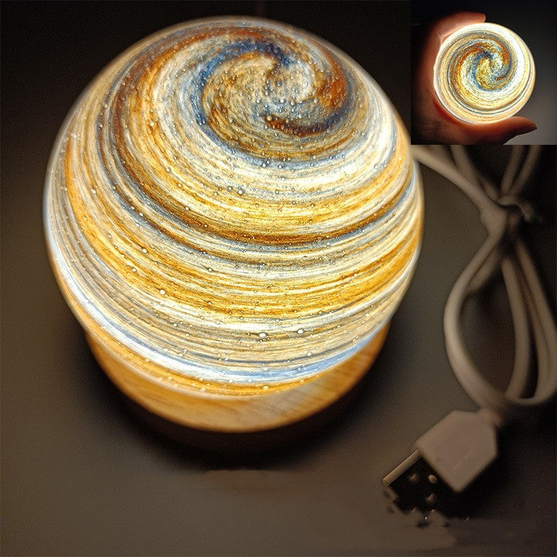 Planet night light in Dawn, a marbled glass globe lit warm on a wooden base