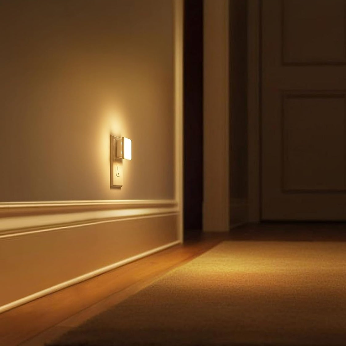 The plug-in night light in a dark hallway, casting a pool of warm light across the floor