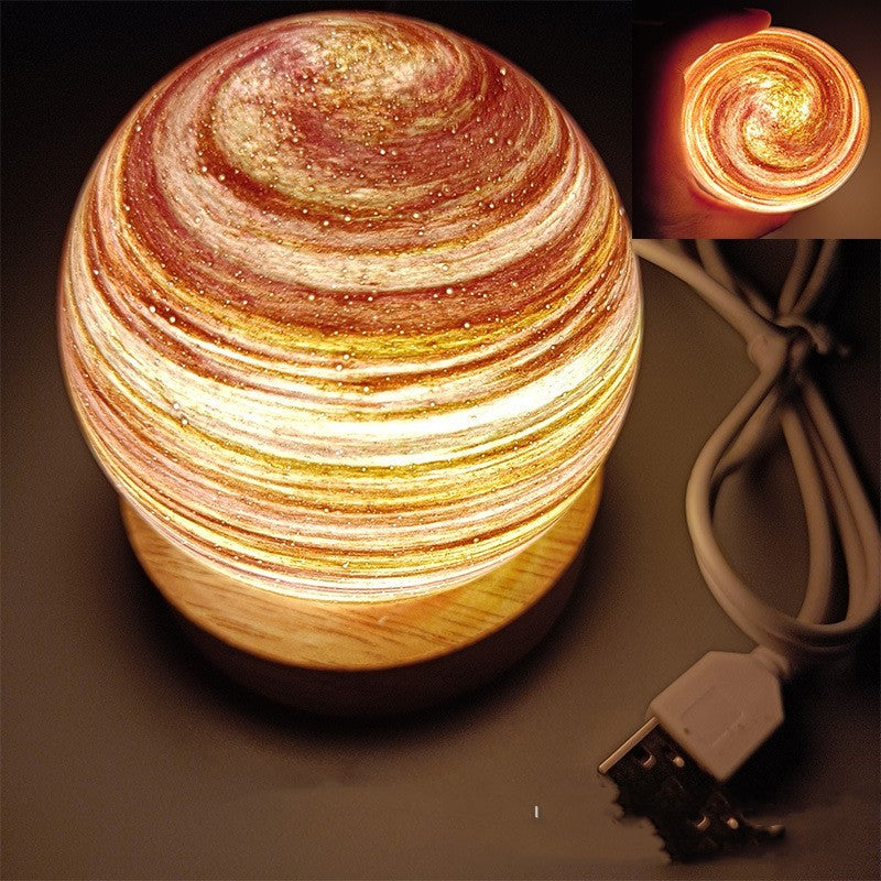 Planet night light in Morning Glow, a marbled glass globe lit warm on a wooden base