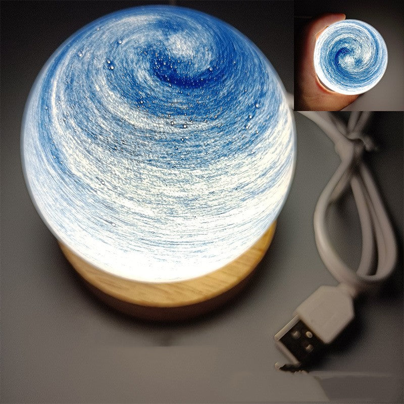Planet night light in Sky Blue, a marbled glass globe lit warm on a wooden base