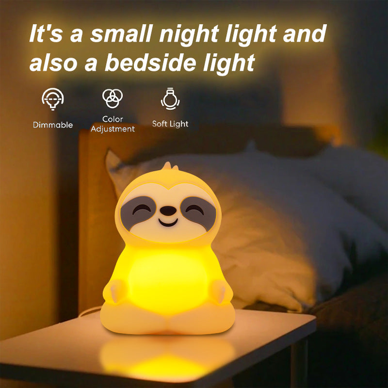 The sloth light glowing warm on a bedside table next to a pillow